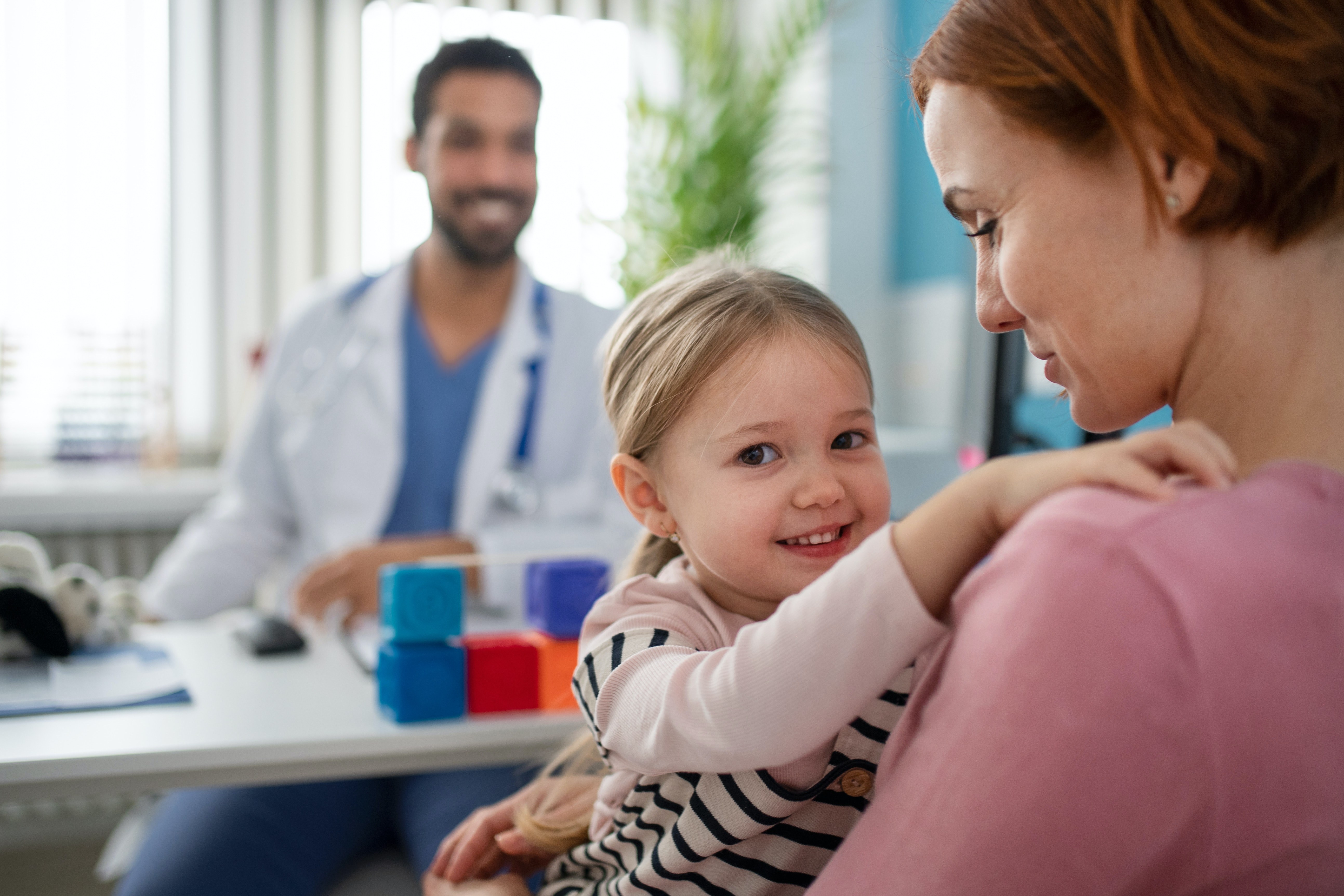 a doctor, a pediatric patient and the patient's mother smiling and conversing